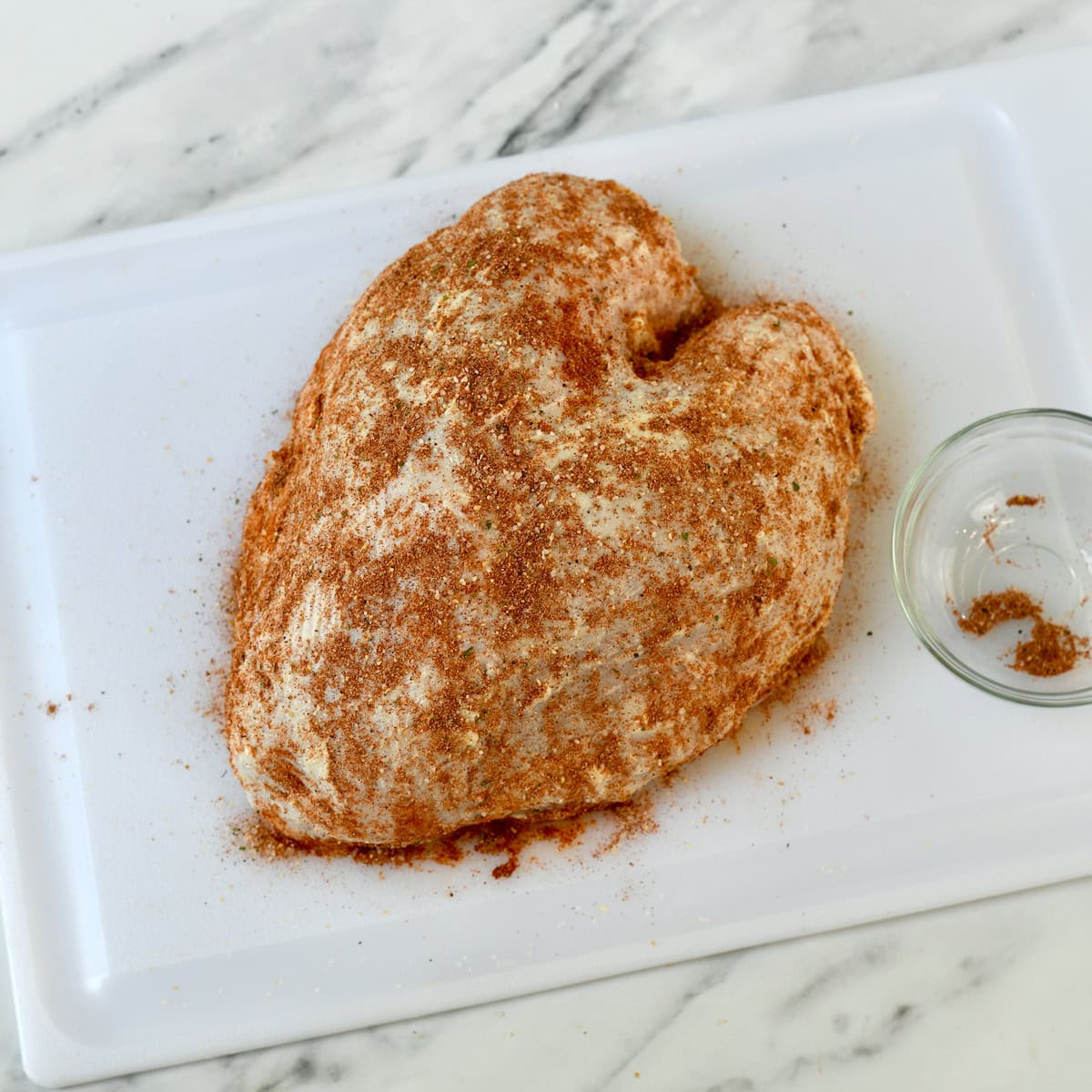 Raw turkey breast with seasonings on it on white cutting board.