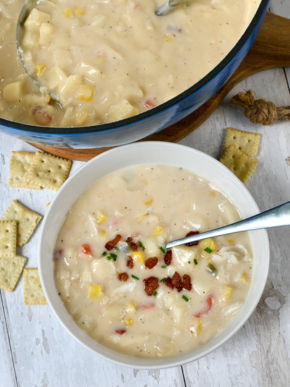 Corn Crab chowder soup in white bowl next to soup in blue pot.