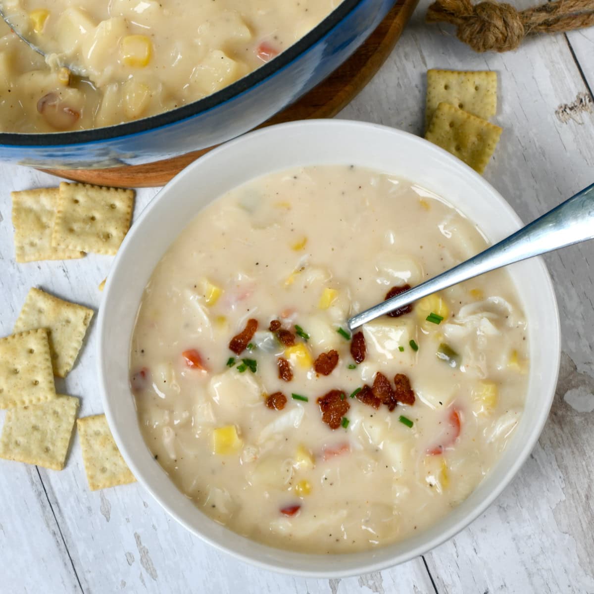 Corn and crab soup in white bowl with spoon in bowl on white surface.