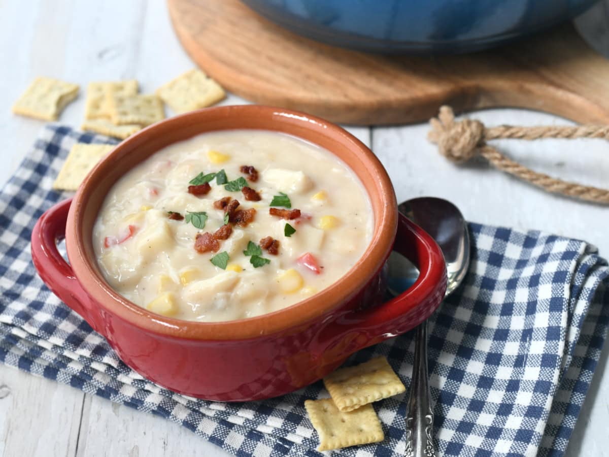 Corn and crab soup in a blow on blue fabric with spoon next to bowl.