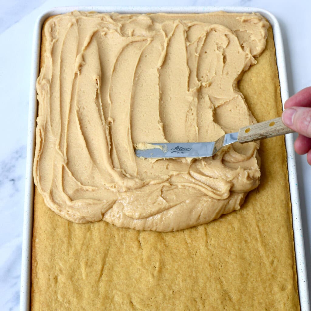 Hand spreading peanut butter frosting on Peanut Butter Sheet Cake.
