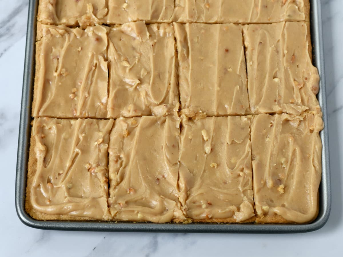 Peanut Butter sheet cake with crunchy peanut butter icing in pan cut into pieces.
