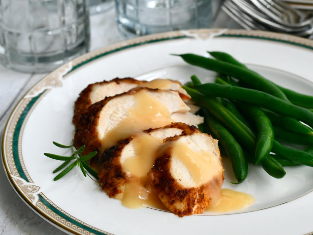 Air fryer turkey breast with gravy sliced on china plate with green beans.
