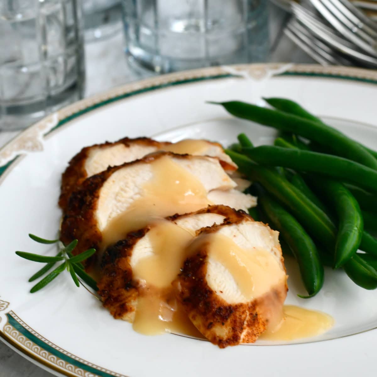Air fryer turkey breast with gravy sliced on china plate with green beans and glasses in background.