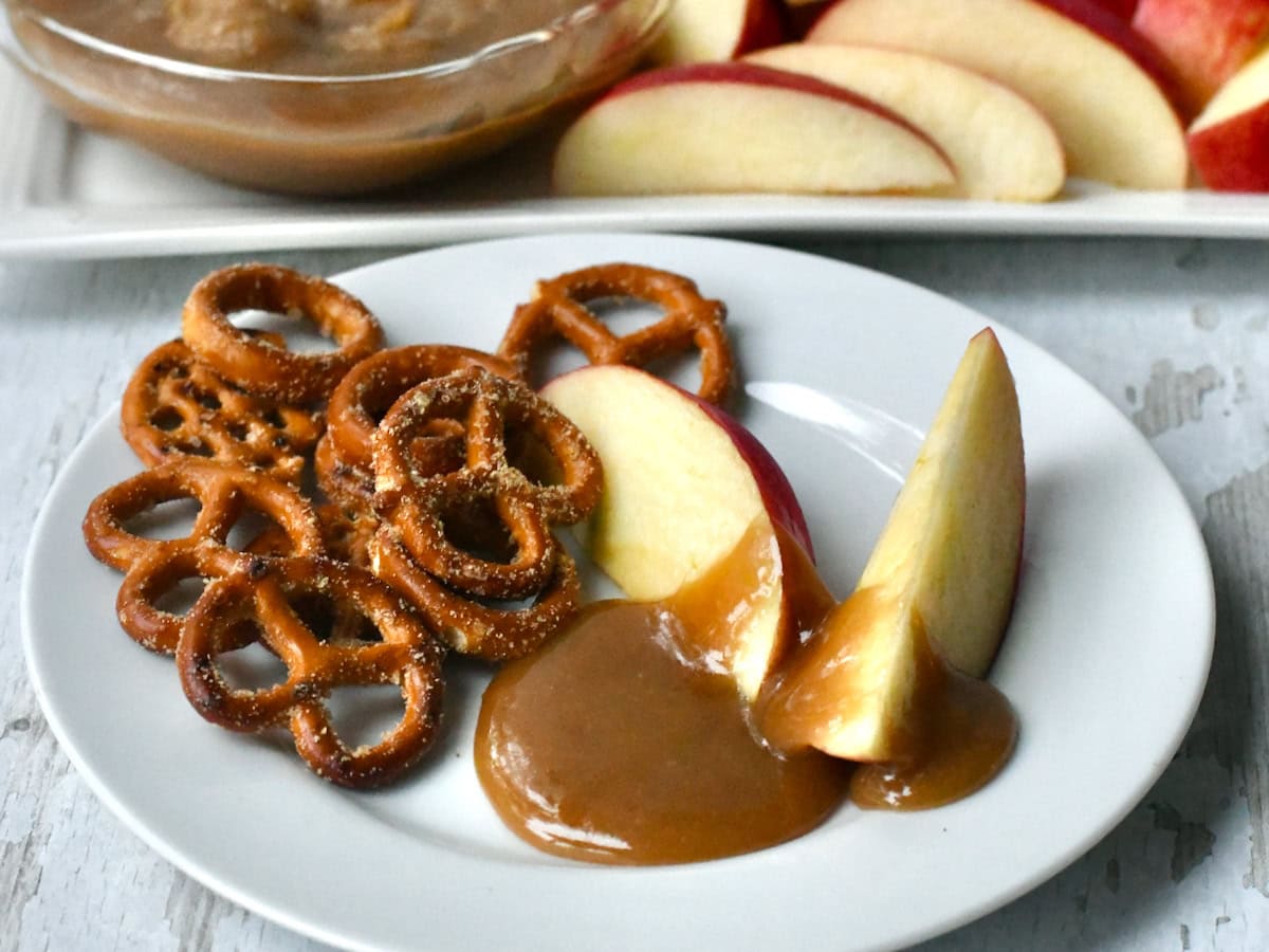 Caramel dip on sliced apples with pretzels on the side of the plate.
