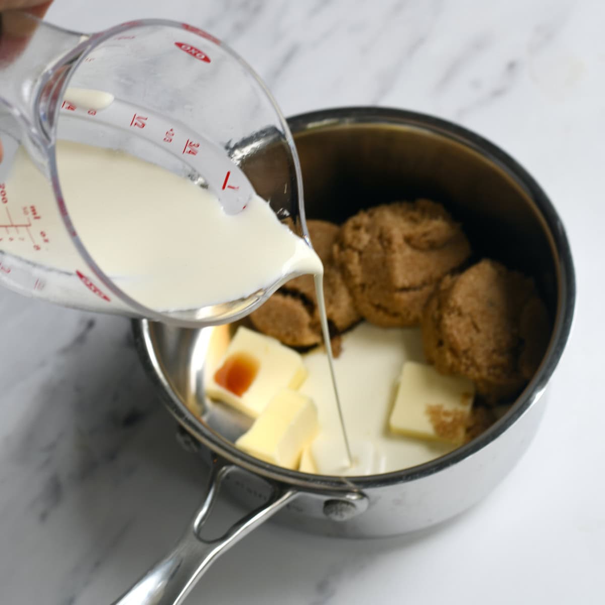 Butter, brown sugar, vanilla in a saucepan where cream is being poured in. 
