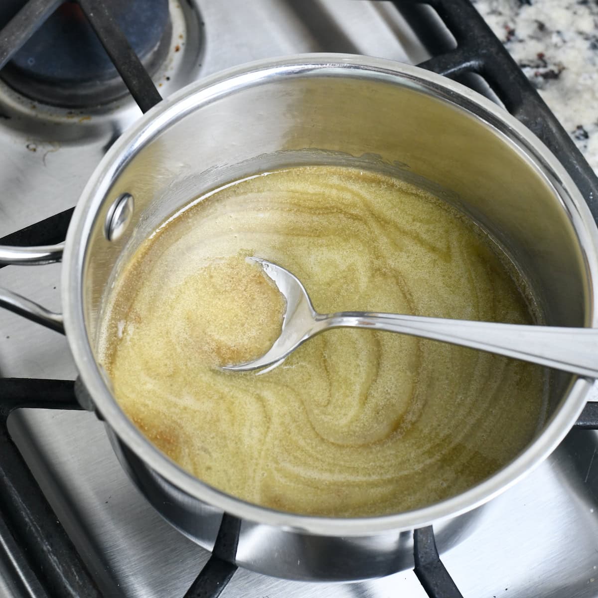 Spoon in a saucepan on stovetop with melted butter and cream in it.
