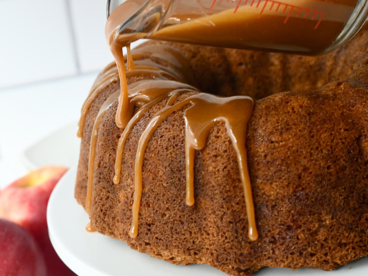 Brown sugar caramel glaze drizzling from a measuring cup onto a fresh apple bundt cake.