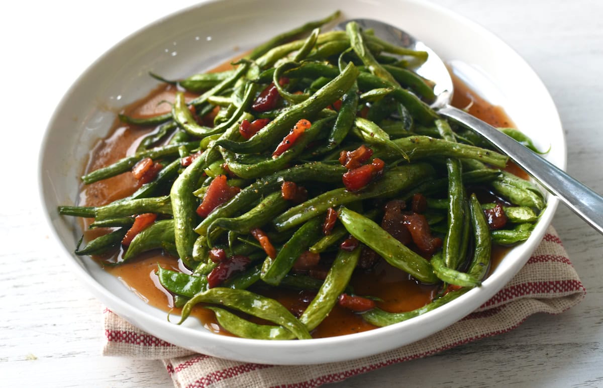 Fresh green beans from the garden with bacon Dales Seasoning on white plate.