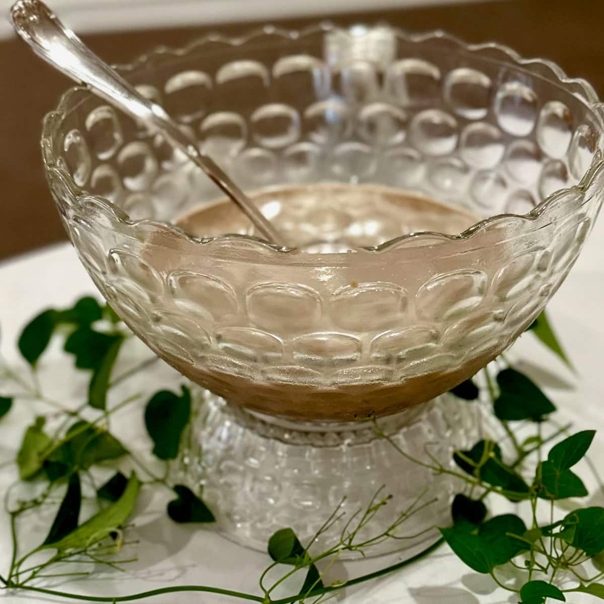 Fostoria punch bowl on stand with greenery around the bottom and coffee punch in the bowl.