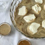Looking down into a punch bowl of mocha coffee punch with swirls of whipped cream and two punch cups.