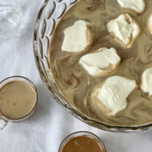Looking down into a punch bowl of mocha coffee punch with swirls of whipped cream and two punch cups.
