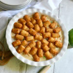 Turkey pot pie topped with tater tots in a pie plate with plates in the background.