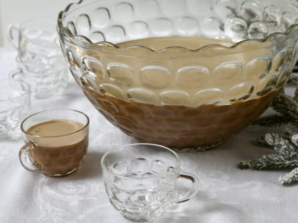 A glass punch bowl filled with creamy coffee punch, with a serving cup beside it
