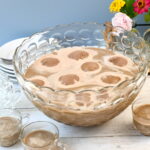 A glass punch bowl filled with creamy coffee punch, topped with scoops of melting ice cream