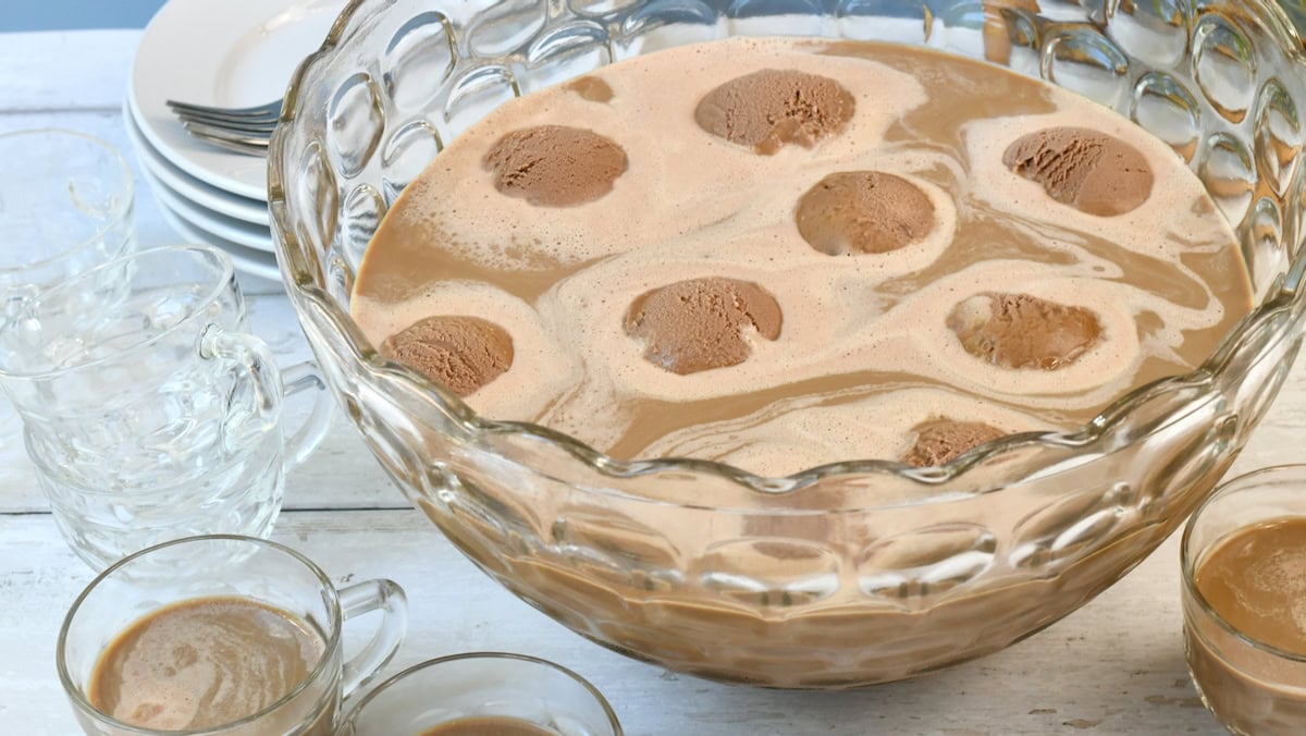 A glass punch bowl filled with creamy coffee punch, topped with scoops of melting ice cream