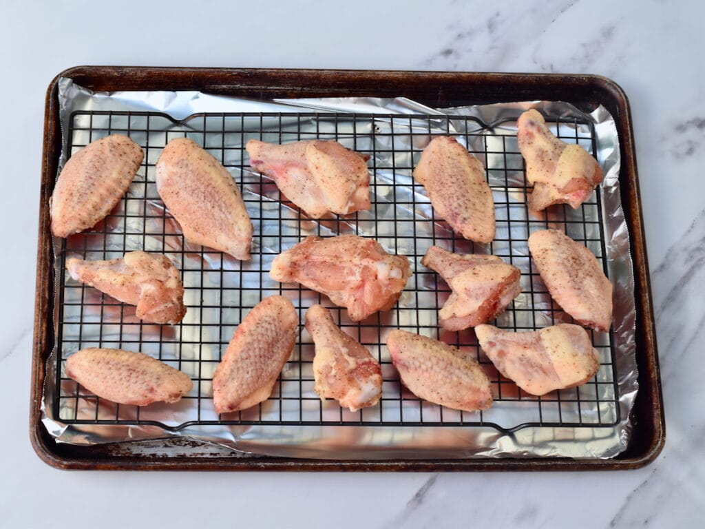 Raw chicken wings seasoned and arranged on a wire rack over a baking sheet