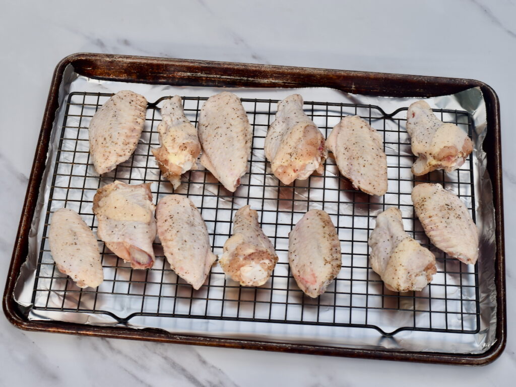 Seasoned raw chicken wings arranged on a wire rack over a baking sheet