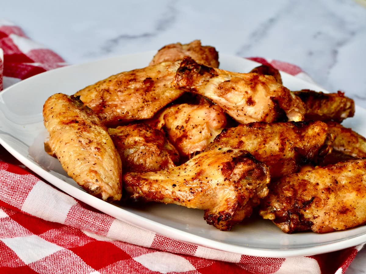 Crispy baked chicken wings on a white plate, set on a checkered tablecloth
