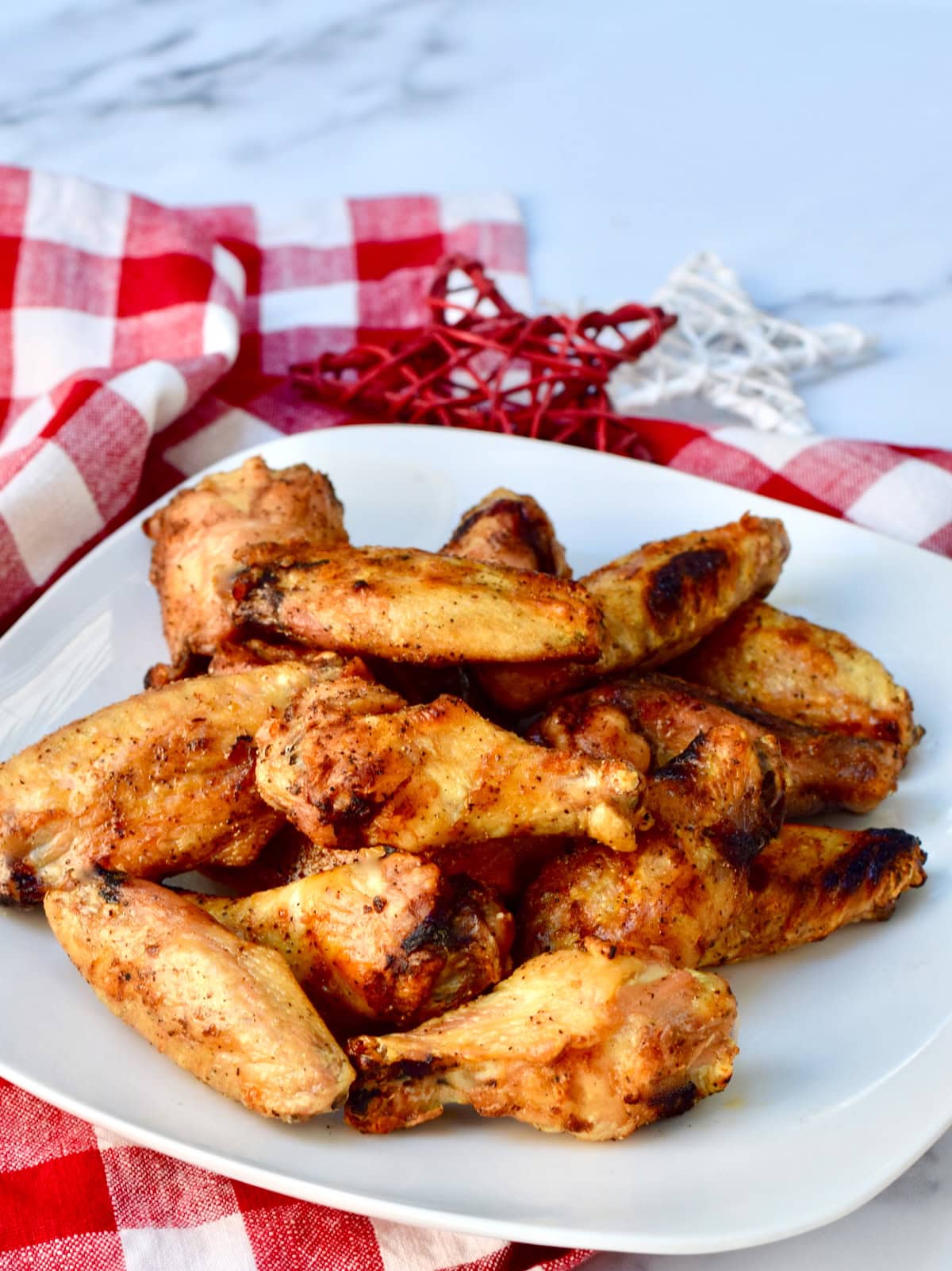 Crispy baked chicken wings on a white plate, set on a checkered tablecloth