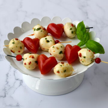 Heart Caprese skewers with mozzarella balls and heart-shaped tomatoes in a small white bowl