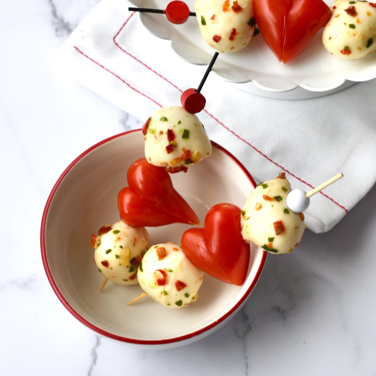Heart Caprese skewers with mozzarella balls and heart-shaped tomatoes in a small white bowl
