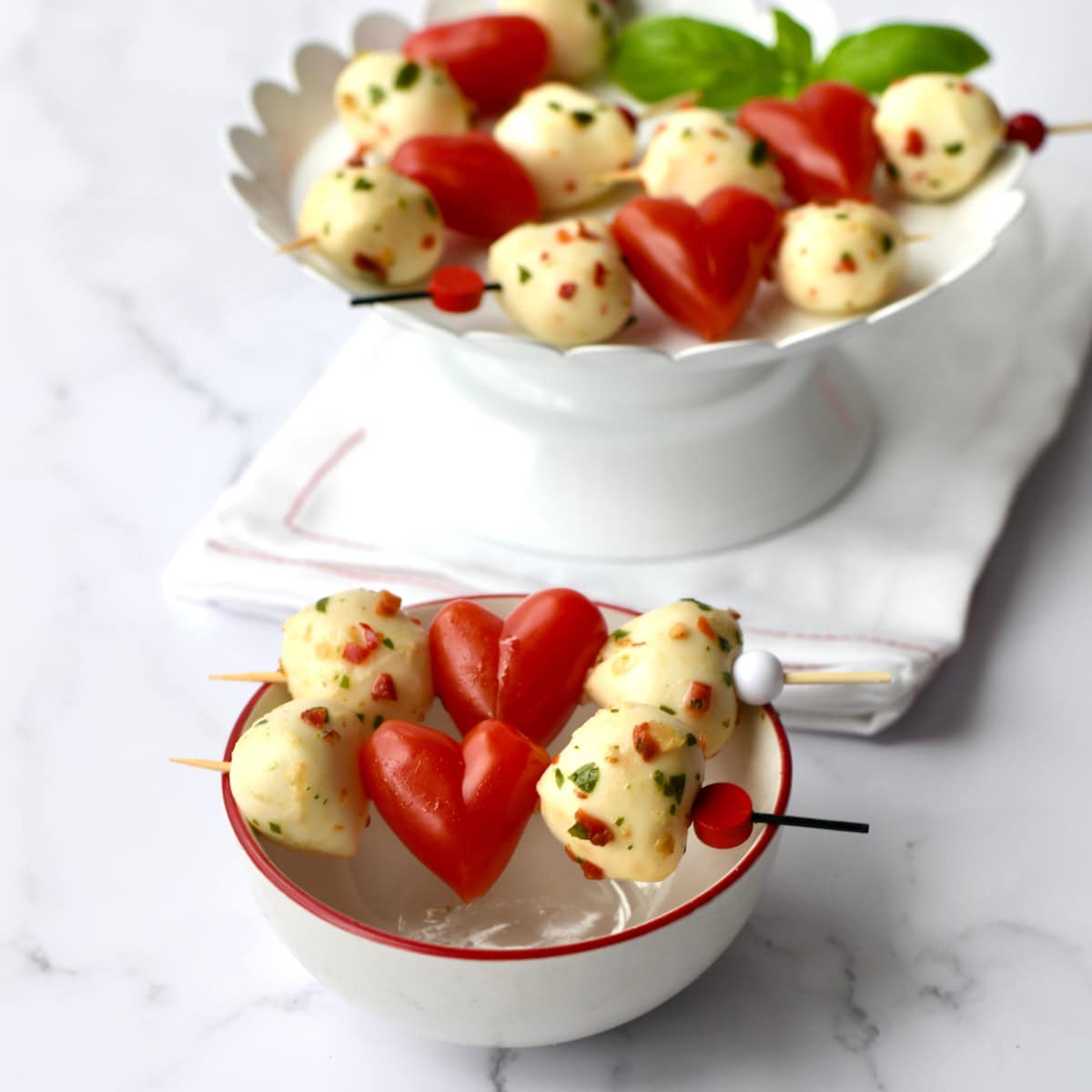 Heart Caprese skewers with mozzarella balls and heart-shaped tomatoes in small white bowls