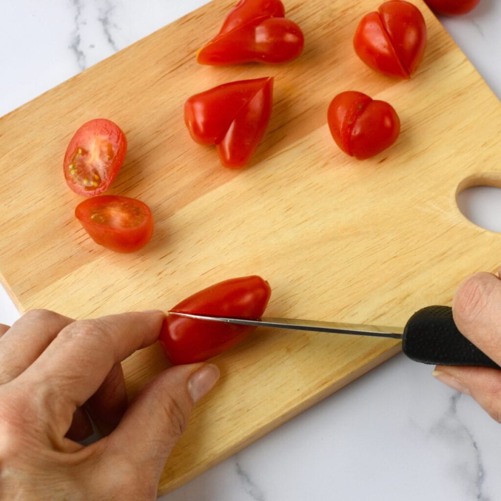 Hands cutting a tomato on a wooden board, shaping it into a heart