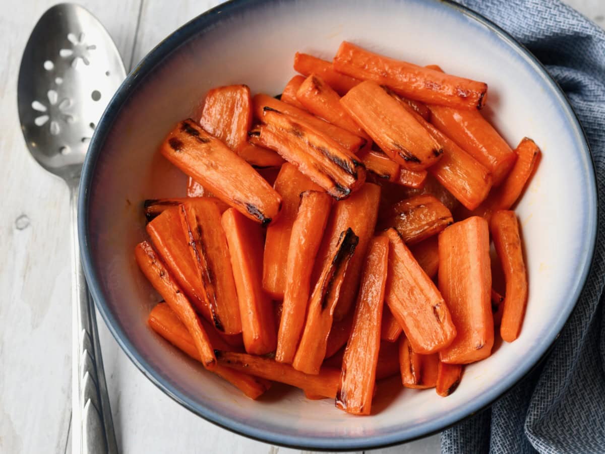 A bowl of air fryer honey roasted carrots, served on a table with a silver spoon
