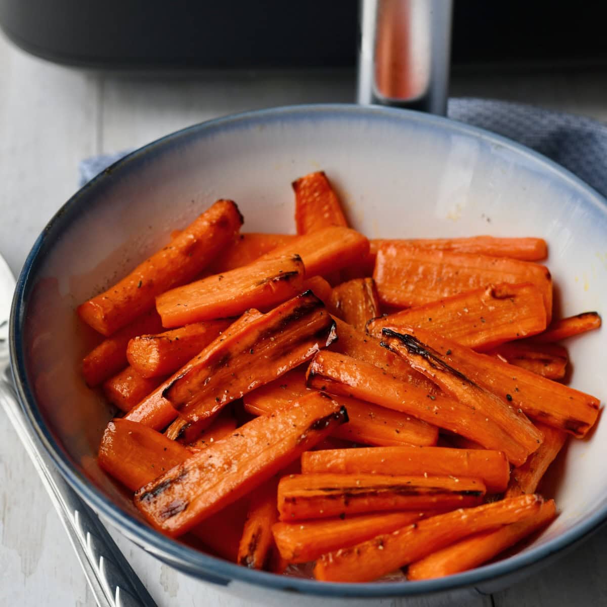 A bowl of air fryer honey roasted carrots, served on a table with a silver spoon