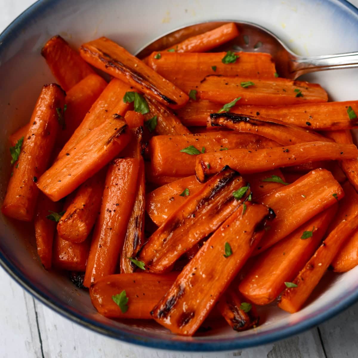 A bowl of air fryer honey roasted carrots garnished with fresh herbs
