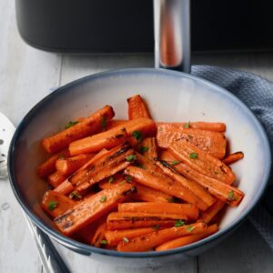 Honey roasted carrot sticks next to an air fryer.