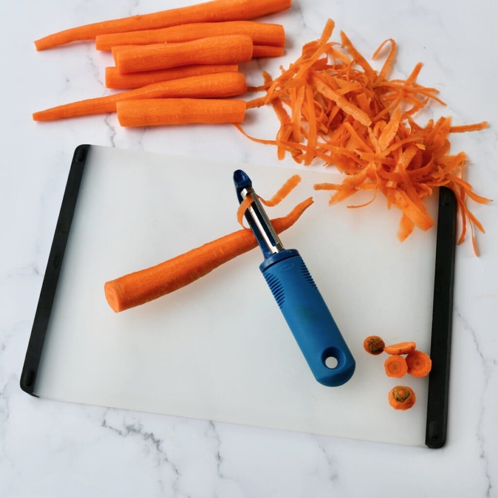 Peeled carrots on a cutting board with a vegetable peeler and carrot shavings
