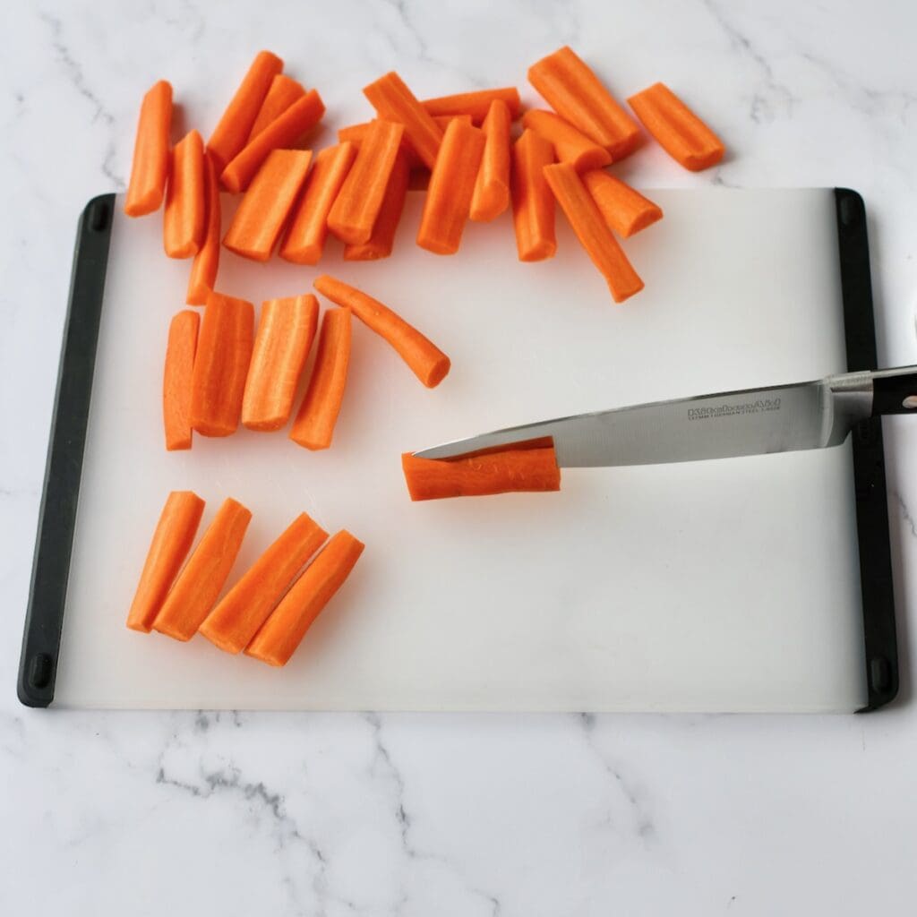 Carrots being cut into evenly sized pieces on a cutting board with a knife

