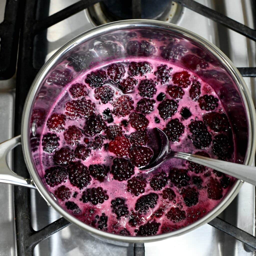 Blackberries simmering in a saucepan on the stove with a spoon