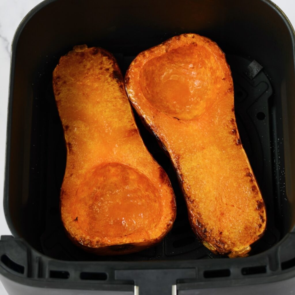 Two butternut squash halves in an air fryer basket