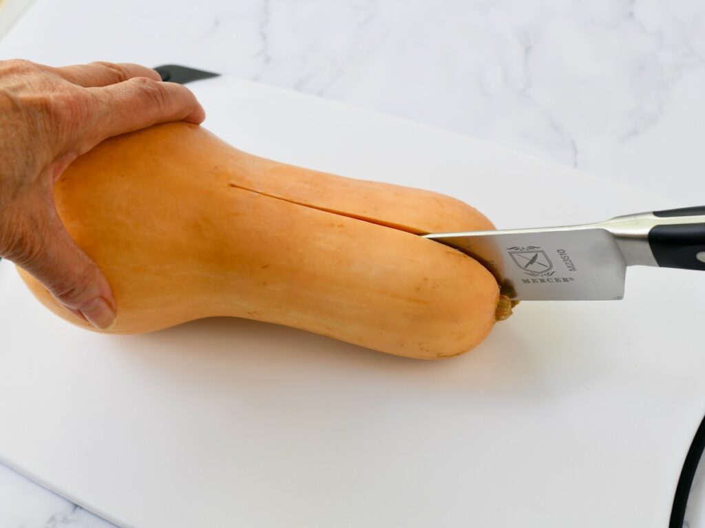 Slicing a whole butternut squash in half on a cutting board