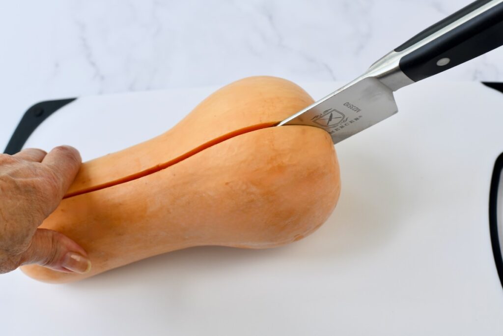 Slicing a whole butternut squash in half on a cutting board