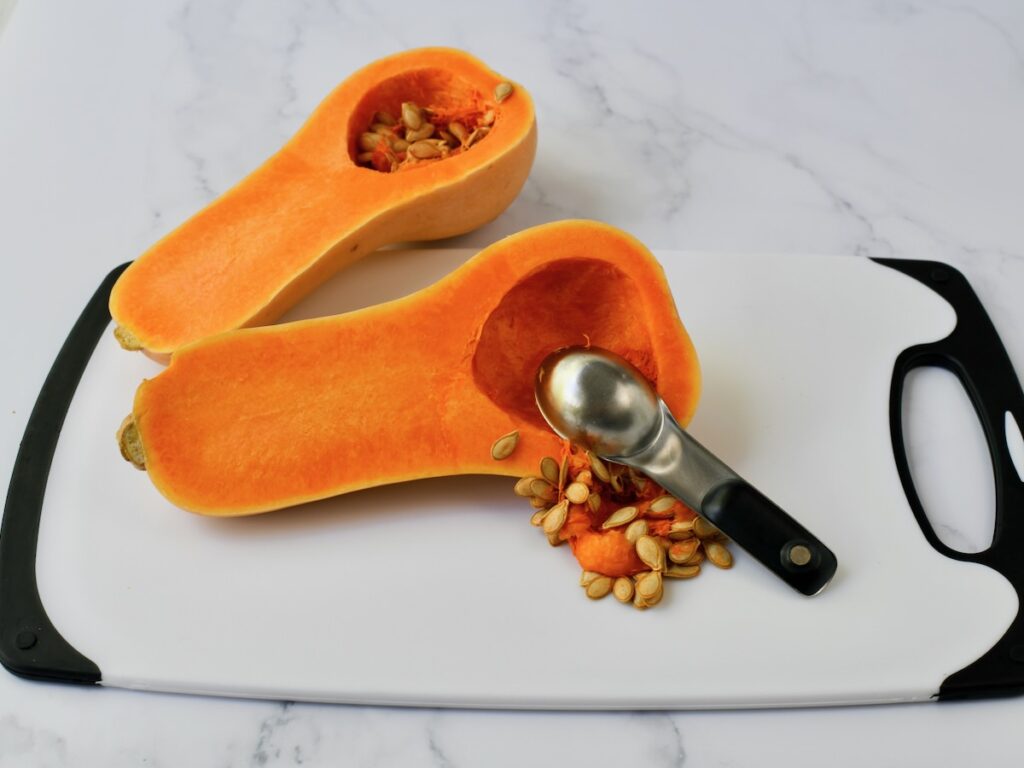Scooping out seeds from halved butternut squash on a cutting board