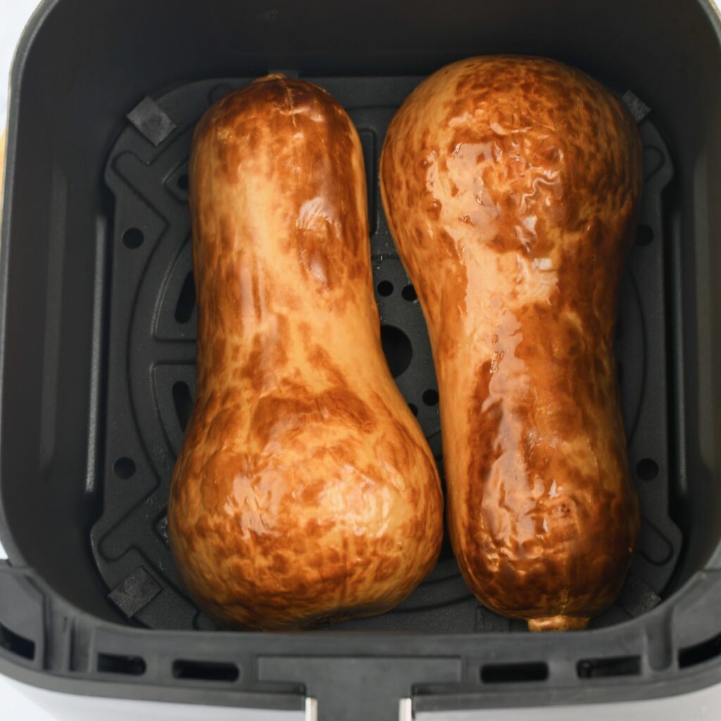 Two butternut squash halves in an air fryer basket
