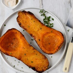 Air fried butternut squash halves on a white plate, garnished with herbs