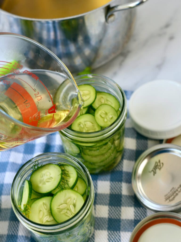 Measuring cup of vinegar pouring into dill pickles in jar.