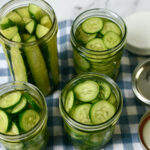 Four jars of pickled cucumbers sit on a table.