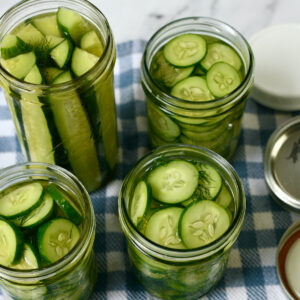 Four jars of pickled cucumbers sit on a table.