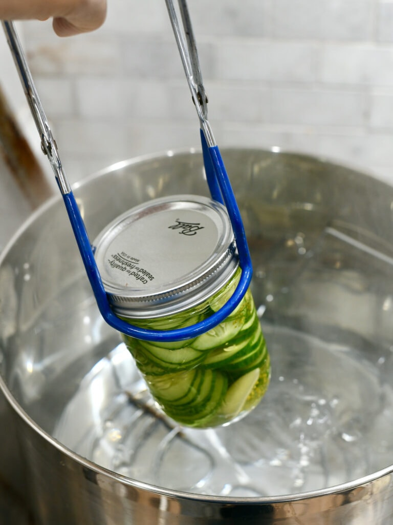 Canning tongs lifting jar out of boiling water in a pot.