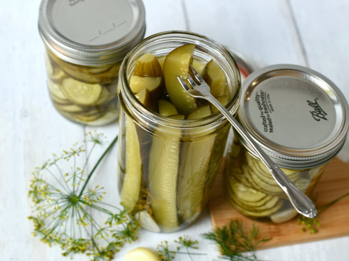 Dill pickle spears in a mason jar with fresh dill and garlic on counter.