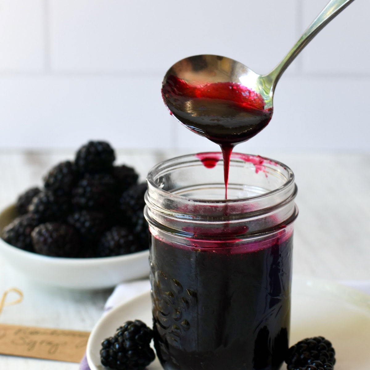 Blackberry syrup dripping from a ladle into a mason jar.
