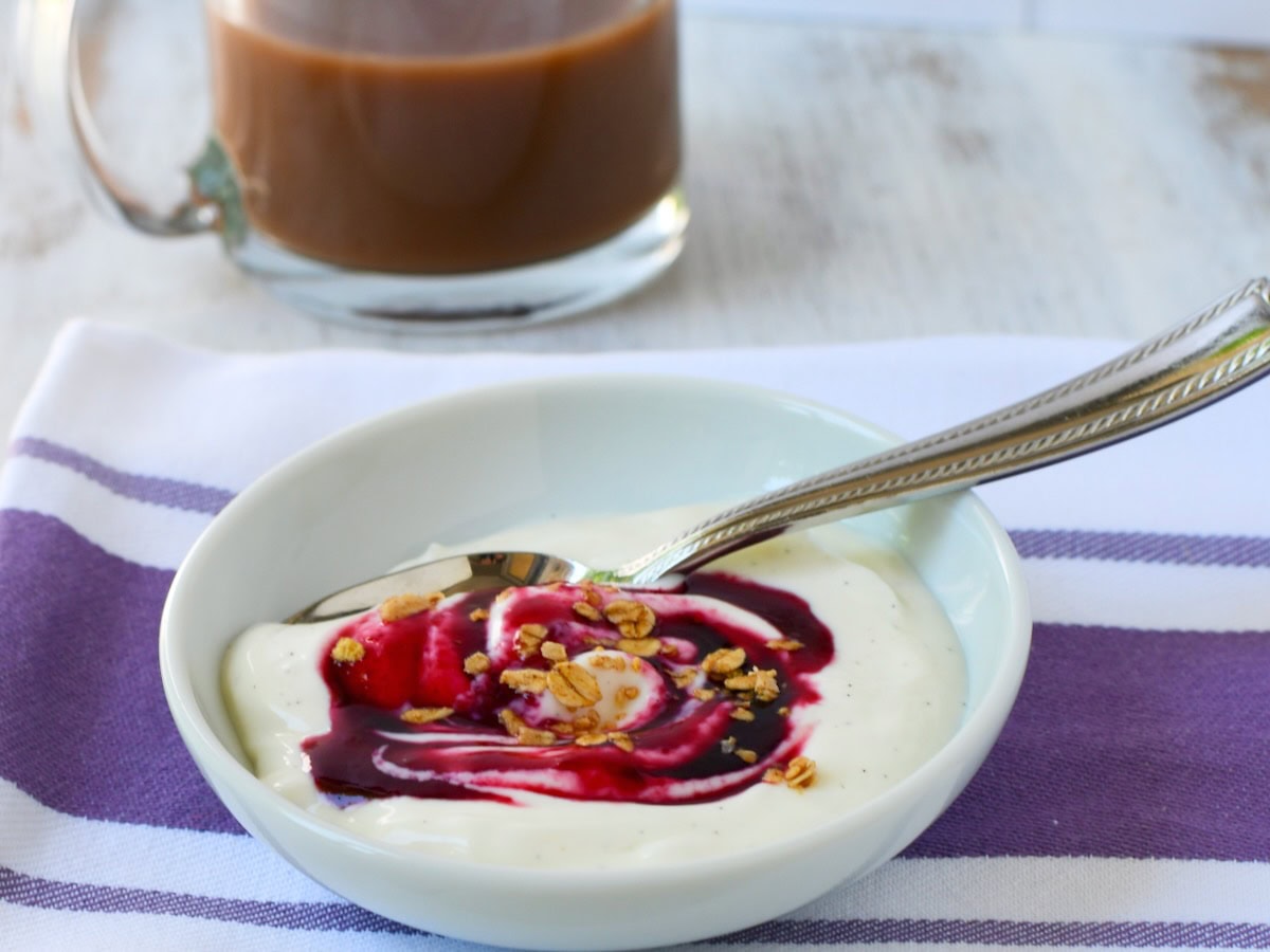 Blackberry syrup swirled into vanilla yogurt in a bowl.
