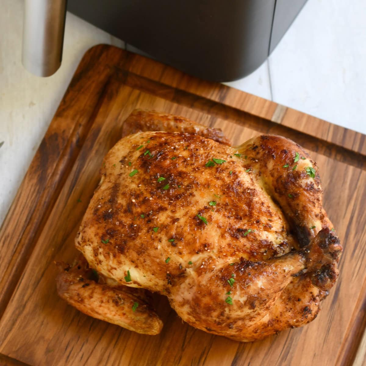 Whole roasted chicken next to a Ninja air fryer on a cutting board.
