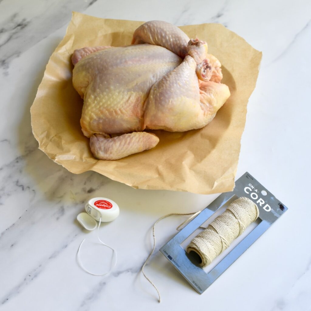 Whole chicken on brown paper with dental floss next to it.
